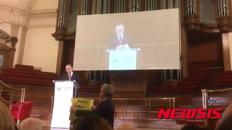 【뉴욕=뉴시스】노창현 특파원 = 영국의 시민단체가 최근 한일위안부협상을 높이 평가한 반기문 유엔 사무총장 앞에서 5일 깜짝 시위를 벌였다. 시위대는 영국 유엔협회 및 채텀하우스가 공동주최한 유엔 70주년 기념식에서 반기문 총장이 연설하기 직전 '위안부를 위한 정의(Justice for Comfort Women)'라는 배너를 약 30초간 들고 있는 퍼포먼스를 감행했다. 행사 시작전에는 건물 입구에서 흰색 저고리와 검정치마를 입은 단발머리 여성이 '살아있는 소녀상' 퍼포먼스를 하고 동료 시위자들이 침묵시위를 벌이며 위안부 문제를 알리는 전단지를 나눠주었다. 사진은 시위자가 반총장을 향해 배너를 들어보이는 장면. 2016.02.05. <사진=Justice4ComfortWomen 동영상 캡처>   robin@newsis.com