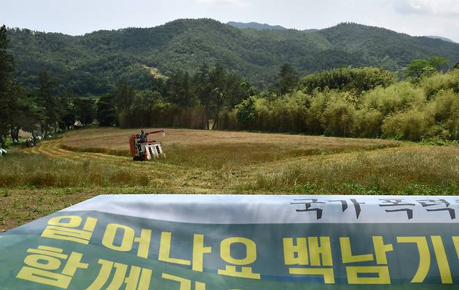 지난 13일 농부 백남기씨의 쾌유를 바라는 펼침막 너머로 콤바인 한 대가 밀을 수확하고 있다. 그는 경찰 물대포에 맞고 쓰러지기 이틀 전(지난해 11월12일) 이 밭에 씨앗을 뿌렸다. 보성/강재훈 선임기자 khan@hani.co.kr