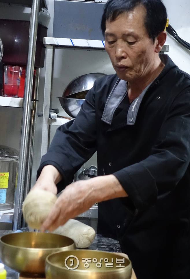 삶아 헹군 냉면 1인분을 손에 사려 그릇에 담고 있다.