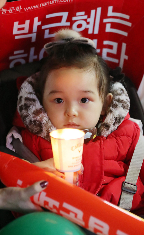 <b > 초롱초롱한 눈망울로… </b> <br> 박근혜 대통령 퇴진을 요구하는 민중총궐기 대회가 열린 지난 12일 서울 광화문광장에서 한 꼬마 아이가 어머니 품에 안겨 초롱초롱한 눈망울로 촛불 너머에 있는 무언가를 응시하고 있다. [한주형 기자]