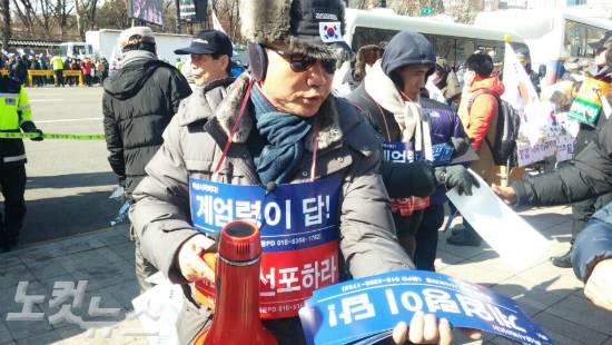 11일 서울시청 앞에서 열린 박근혜 대통령 탄핵 반대 집회 참가자가 '계엄렴이 답! 계엄령 선포하라'고 적힌 손팻말을 나눠 주고 있다. (사진=이진욱 기자)