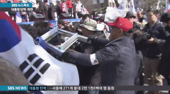 태극기집회 참가자가 취재용 철재 사다리로 취재중인 기자를 내려치고 있다.