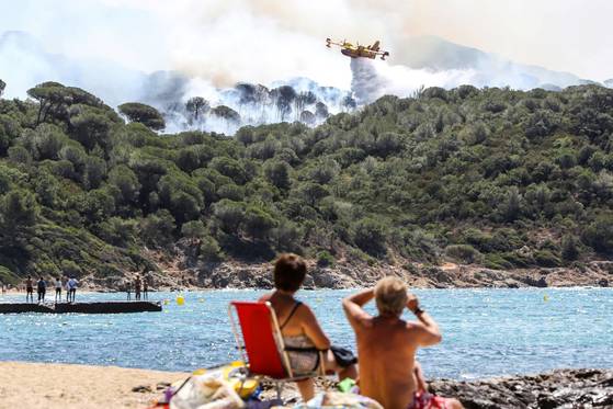 상트로페 인근 해변에서 휴양객들이 25일(현지시간) 가까운 산 위로 치솟은 불길을 바라보고 있다. [AFP=연합뉴스]