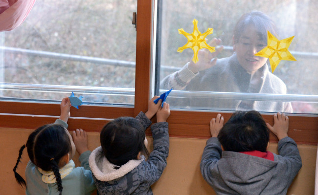 한 학부모가 어린이집에서 놀고있는 아이를 창 박에서 지켜보고 있다.