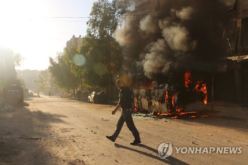 25일 시리아 알레포의 한 주민이 시리아군의 폭격에 불타는 버스 옆을 지나고 있다. [AFP=연합뉴스]