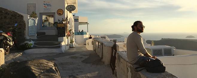 지난 달 25일 그리스 산토리니 피라마을에서 한 관광객이 길 옆 낮은 담장에 걸터 앉아 바다를 바라보고 있다.