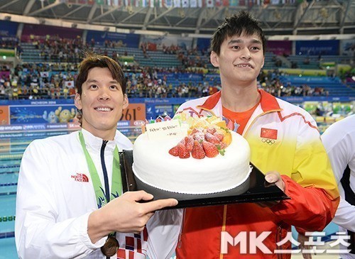 박태환(왼쪽)이 인천아시아경기대회 혼계영 4x100m 시상식 종료 후 쑨양(오른쪽)에게 받은 생일케이크를 가리키며 웃고 있다. 사진(문학박태환수영장)=MK스포츠 DB