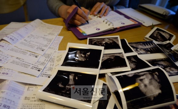 박씨가 그동안의 입원 진료비계산서를 꺼내 그동안 든 비용을 기입하고 있다. 그 주변에 뱃속 아이의 사진들이 펼쳐져 있다.