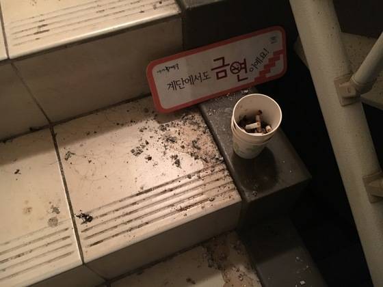 담배꽁초가 담긴 종이컵이 금연 안내 팻말 바로 앞에 놓여 있다. 주변에 담뱃재도 흩어져 있다. 백수진 기자