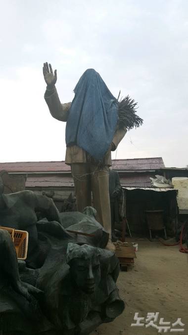 서울 마포구 박정희 기념 도서관에 설치 예고된  박정희 동상. 도서관에서 불과 7km 떨어진 곳에 비밀리에 보관중이다. 머리 부분을 천으로 덮은데다 왼쪽 품에 볏단이 안겨 있어 일견 닭의 모습을 연상시키는 '반인반수' 형상이다.