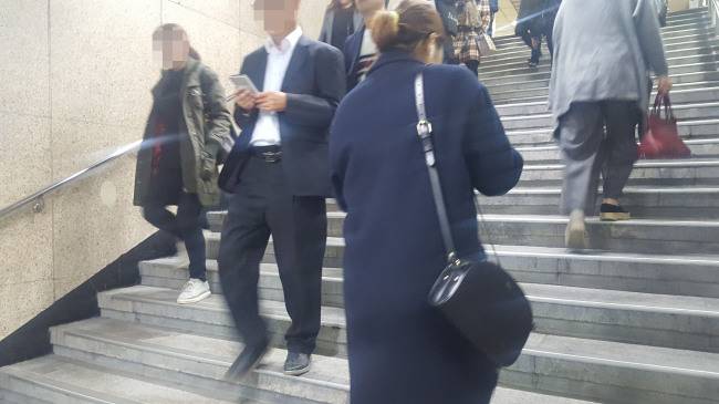한 남성이 스마트폰에 눈길을 주며 지하철역 내 계단을 내려가고 있다.