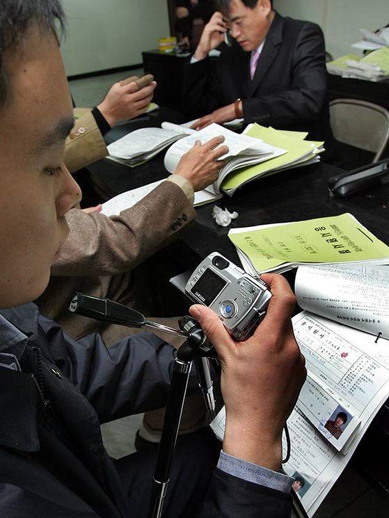 2004년 수능 휴대전화 부정행위 발생 후 충남지방경찰청 소속 경찰들이 대전시교육청에서 대리시험 여부 확인을 위해 응시원서의 증명사진과 주민등록번호 등을 촬영하고 있다. [중앙포토]