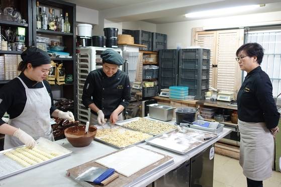 두 직원이 크림 트뤼플 초콜릿 만드는 걸 지켜보고 있는 고영주 대표(오른쪽). 화이트 바닐라 초콜릿으로 속을 만들고 녹인 다크 초콜릿에 담가 겉을 씌운 뒤 아몬드 슬라이스에 굴리는 과정이다.