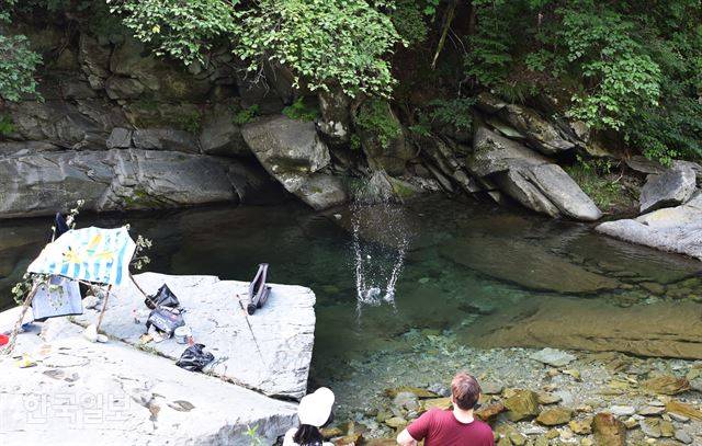 한 커플이 계곡 바위에 큰 수건으로 그늘을 만들고 물수제비 장난을 하고 있다.