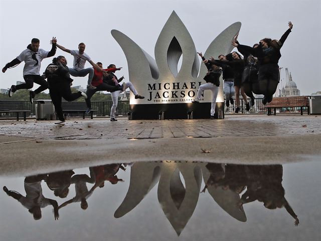 고(故) 마이클 잭슨의 60번째 생일 맞은 29일(현지시간) 영국  런던의 명소 사우스뱅크에서 잭슨의 팬들이 잭슨의 다이아몬드 생일을 축하하기 위해 설치한  거대한  왕관 앞에서 포즈를 취하고 있다. AP 연합뉴스