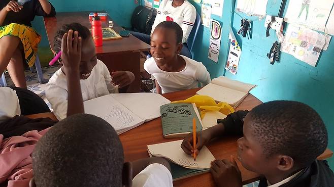 케냐 미고리주 쿠리아의 ‘미스차나 도서관’에서 진행된 방과후 활동에 참가한 여성청소년들이 영어단어 받아쓰기 시험을 본 뒤 서로 문제를 채점해주며 웃고 있다.