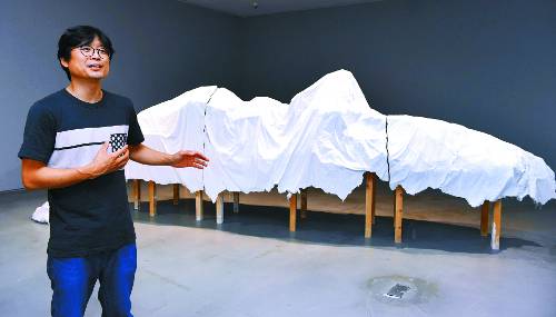 권용주 작가가 지난 7월 말 개인전 ‘캐스팅’이 열린 서울 종로구 두산아트센터 두산갤러리에서 작품에 대해 이야기하고 있다. 뒤로 보이는 작품이 쓰레기 구조물에 포장 천막을 씌운 뒤 그 전체를 석고로 형을 뜬 ‘포장 천막3’이다. 최종학 선임기자