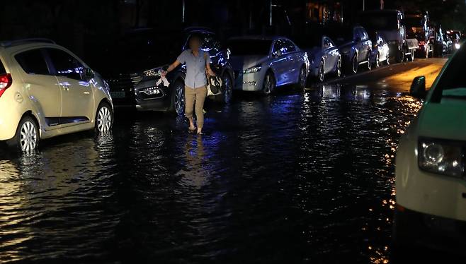 지난달 11일 오후 해수면 상승으로 경남 창원시 마산합포구 해운동 일대 도로에 물이 유입돼 한 시민이 양말과 신발 등을 손에 들고 걷고 있다.[연합뉴스]