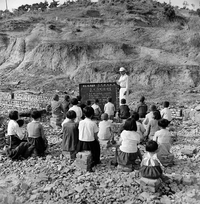 1950년 폐허가 된 학교터에서 유엔환영가를 배우고 있는 학생들. [사진 국가기록원]