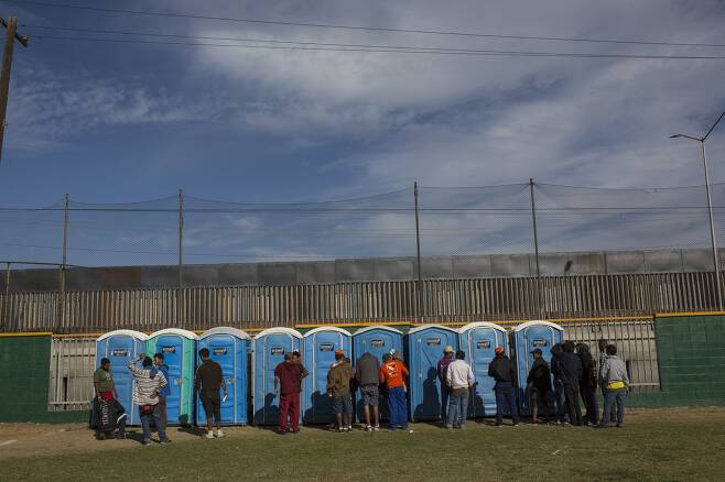 캐러밴 이민자들이 18일(현지시간) 멕시코 티후아나 시 임시 보호소에서 화장실 앞에 줄을 서 있다.[AP=연합뉴스]