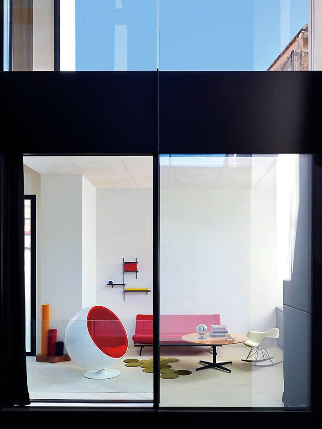 창문을 통해 보이는 1층 거실. 오스발도 보르사니가 디자인한 소파와 테이블 양쪽으로 에어로 아르니오의 ‘볼’ 체어와 찰스 & 레이 임스가 디자인한 흔들의자를 배치했다. 카펫은 부홀렉 형제가 갤러리 크레오(Galerie Kreo)와 협업한 제품이다.