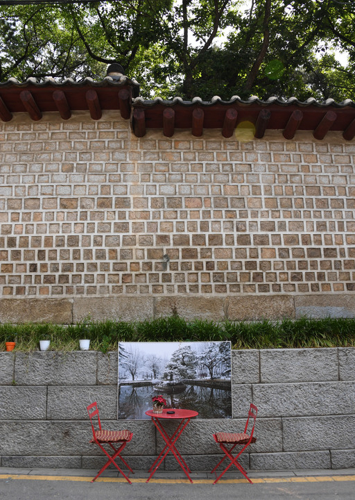 종묘 연못 사진이 붙은 서울 종로구 서순라길 돌담 아래 빨간 테이블과 의자가 놓여있다. 이 자리는 노천 술집 ‘예카페’의 한 좌석으로, 넷플릭스 영화 ‘페르소나’에서 아이유와 정준원이 와인을 마시던 자리다. 이제원 기자