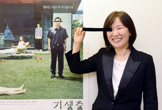 곽신애 대표가 자신의 사무실 벽에 붙여놓은 ‘기생충’ 포스터 옆에 서서 포스터 속 배우들처럼 검은 띠로 눈을 가리고 있다. 곽 대표는 “이 영화를 통해 처음으로 함께 만들어가는 기쁨을 맛봤다”고 말했다.  신창섭 기자 bluesky@