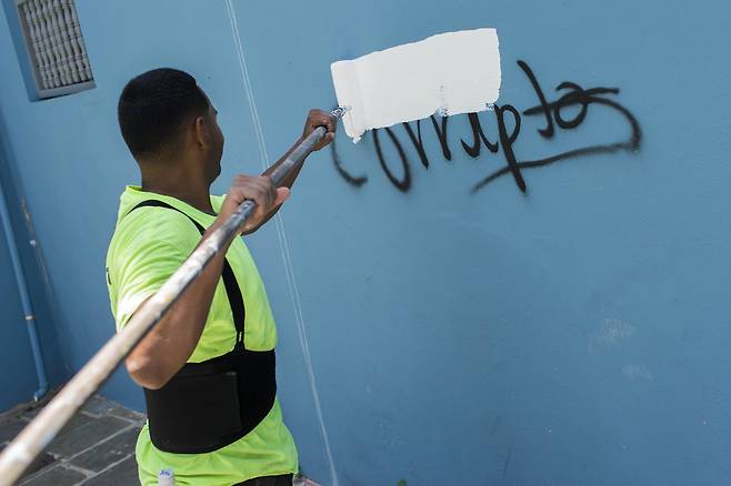 18일 한 남성이 벽에 써 있는 "Corrupt" 란 단어를 흰색 페인트로 덮고 있다. 스페인어로 corrupt는 부패를 의미한다. [AP=연합뉴스]