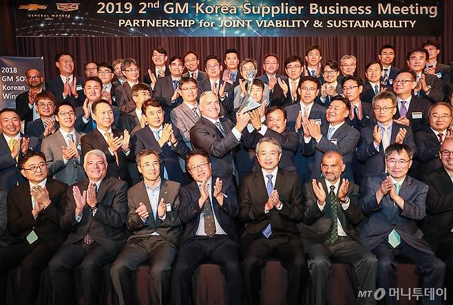 한국GM이 지난 24일 서울 메이필드 호텔에서 개최한 '2019 협력사 초청 경영현황 설명회'에서 기념촬영하는 모습. 스티븐 키퍼(Steven Kiefer) GM 글로벌 구매 부사장(트로피를 중심으로 왼쪽)과 문승 한국GM 협신회 회장이 트로피를 들어보이고 있다. /사진제공=한국GM