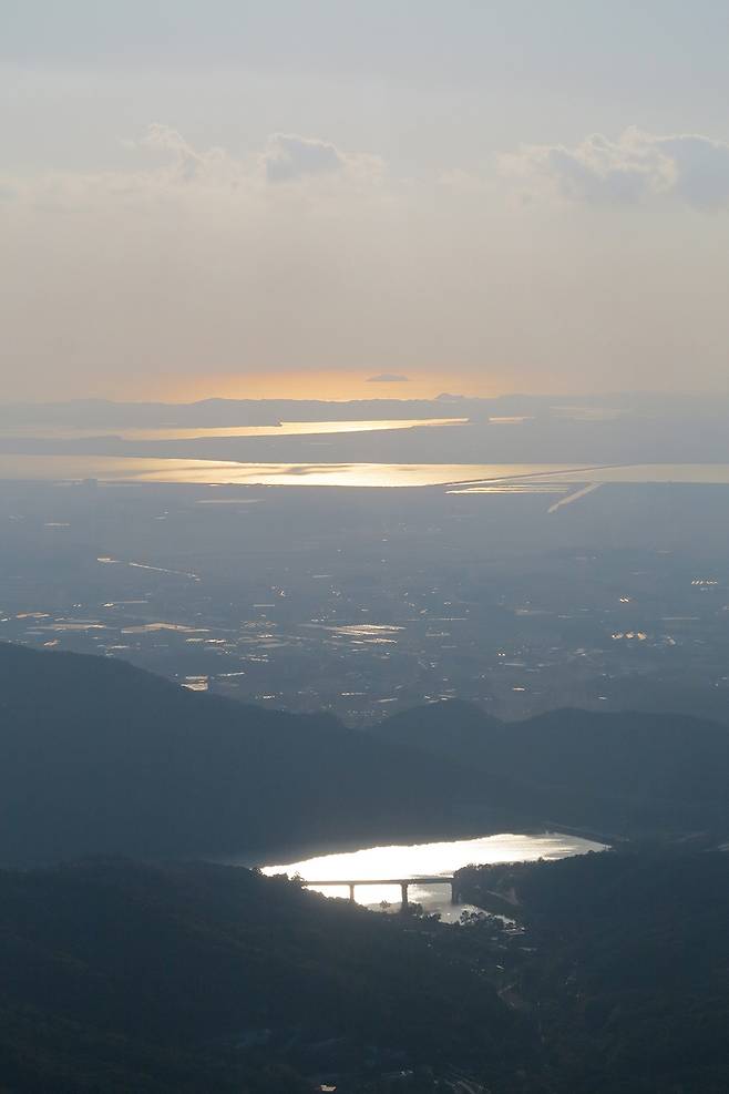 석문봉에서 서쪽으로 내려다 본 서산시 해미읍 산수저수지. 산수저수지 뒤 멀리는 바닷물인 간월호와 부남호. 부남호 뒤 육지처럼 길게 보이는 곳은 안면도와 태안반도이다. 태안반도 뒤는 저녁노을을 기다리는 서해바다이다.