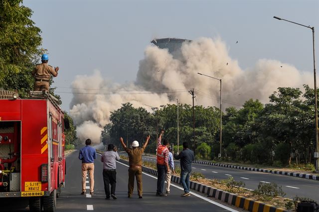 인도 아마다바드에서 약 40km 떨어진 간디나가르 외곽에서 1일(현지시간) 구조요원들이 인도에서 두번째로 높은 118m의  구자라트주 화력발전소 쌍둥이 냉각탑이 붕괴되는 모습을 바라보고 있다. AFP 연합뉴스