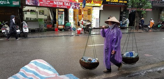 비 오는 거리에 물건을 어깨에 메고 가는 하노이 시민.