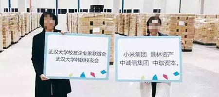 한국서 공수된 마스크 박스 - 중국 우한대 한국총동문회 간부가 한국에서 공수한 마스크·방역 물자 앞에서 물자 조달에 참여한 단체·기업명이 쓰인 피켓을 들고 기념 촬영을 하고 있다. 왼쪽 피켓에는 우한대 동문 단체들, 오른쪽에는 샤오미그룹 등 기업명이 적혀 있다. /인터넷 캡처