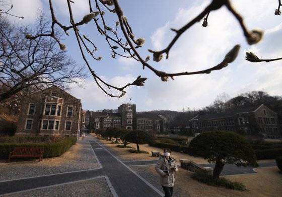 2일 서울 서대문구 연세대학교 본관 목련 꽃봉오리 앞으로 마스크를 쓴 학교 관계자가 지나가고 있다.   신종 코로나 바이러스 감염증(코로나19)으로 인해 16일로 개강이 연기되면서 각 대학은 온라인 강의 등 원격 강의 시행을 준비하고 있다. [연합뉴스]