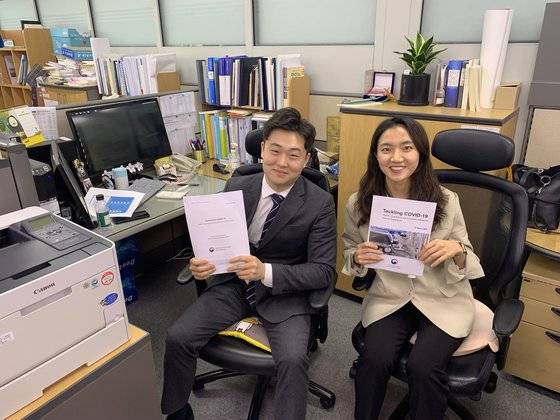 기획재정부 개발금융총괄과 박준석ㆍ이현지 수습 사무관(왼쪽부터)이 사무실에서 포즈를 취했다. 손에 든 건 세계은행(WB)을 통해 개발도상국에 보낸 신종 코로나 국내 대응 소개 자료다. [기재부]