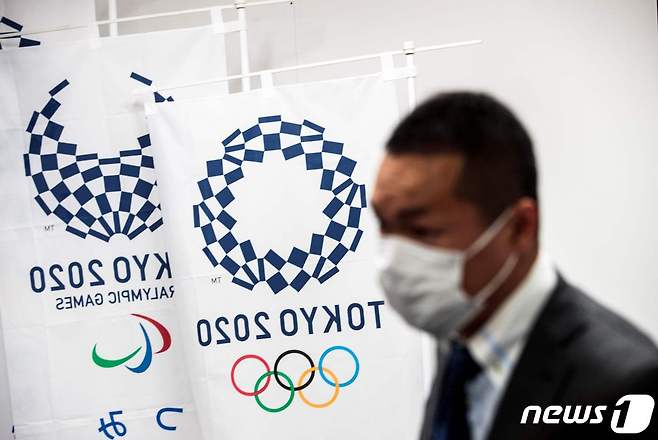 先月 11日日本東京で開かれた記者会見でマスクをかけた記者が東京オリンピック垂れ幕横に立っている. (C) AFP=ニュース1