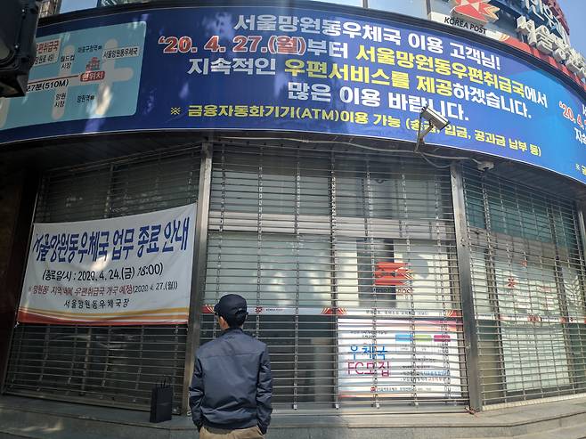 4월 27일 서울 마포구 망원동우체국 앞에서 한 시민이 우체국 폐국을 안내하는 현수막을 보고 있다./김태훈 기자