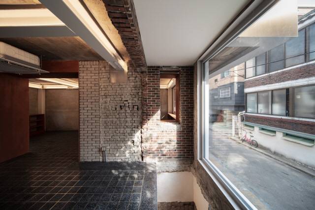 1층 내부 살롱 메인 창 옆의 벽면은 세 가지 마감이 혼재하고 있다. 적벽돌이 있는 부분은 원래 외벽이었던 곳으로 과거 확장의 흔적이다./사진제공=에스티피엠제이