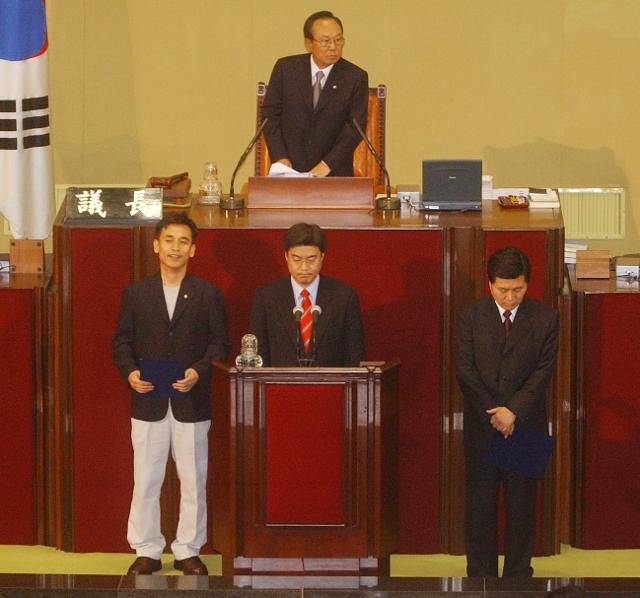 2003년 4월 29일 서울 여의도 국회 본회의장에서 유시민(왼쪽) 국민개혁정당 의원이 흰색 면바지 차림으로 의원선서를 하기 위해 단상에 서 있다. '복장 불량'을 지적하는 의원들의 질타가 이어지자 함께 나온 오경훈, 홍문종 의원이 고개를 숙이고 있다. 한국일보 자료사진