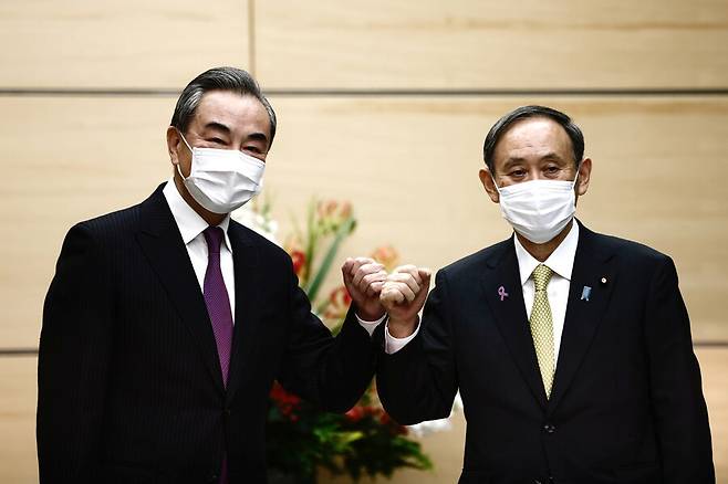 스가 요시히데(오른쪽) 일본 총리가 25일 방일 중인 왕이 중국 외교담당 국무위원 겸 외교부장을 도쿄 총리관저에서 만나 주먹인사를 하고 있다. 도쿄/로이터 연합뉴스
