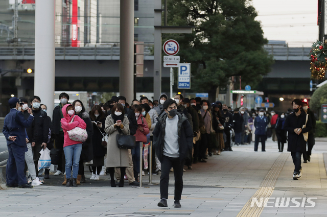 [도쿄=AP/뉴시스]지난 10일(현지시간) 일본 도쿄에서 한 남성(가운데)이 복권을 사기 위해 줄을 서서 기다리는 사람들을 지나쳐 걸어가고 있다. 2020.12.10.