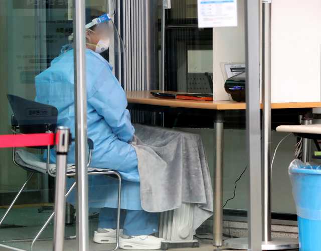 22일 서울 국립중앙의료원 선별진료소에서 한 관계자가 전기 라디에이터와 무릎 담요로 추위를 피하고 있다. 뉴시스