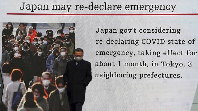 코로나19 확산에 의한 긴급사태 선포가 임박한 일본 도쿄의 거리에서 마스크를 쓴 한 남성이 관련 내용이 보도된 스크린 앞을 걸어가고 있다.  도쿄 | AP연합뉴스