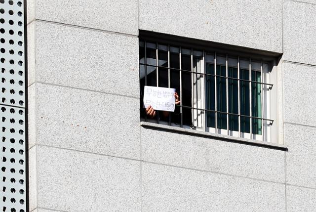 An inmate at Dongbu Detention Center in Seoul shows a piece of paper to reporters outside the window that reads “Incompetent president and incompetent ministry of justice,” on Wednesday. (Yonhap)