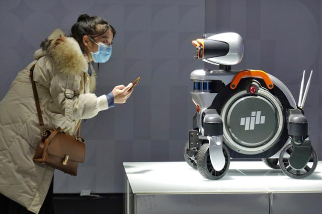 지난해 11월 중국 산둥성 옌타이에서 열린 세계 산업디자인 전시회에서 마스크를 쓴 여성이 순찰 로봇을 유심히 살펴보고 있다. 옌타이=AP 연합뉴스