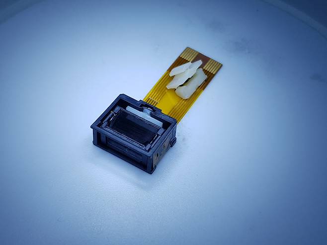 마이크로엑츄에이터가 개발한 폴디드 줌 OIS와 액추에이터 지지구조 부품(연성기판위에 흰색 구조물).