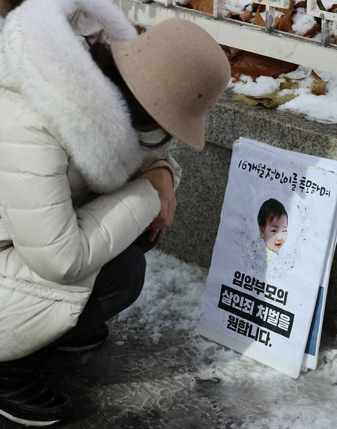 16개월 된 입양 딸 정인 양을 학대해 숨지게 한 혐의를 받는 양부모의 첫 재판이 열린 13일 서울 양천구 남부지방법원에서 재판이 끝난 뒤 한 시민이 법원 청사 앞에 놓인 정인 양의 사진 앞에서 정인 양을 추모하고 있다 (사진=연합뉴스)