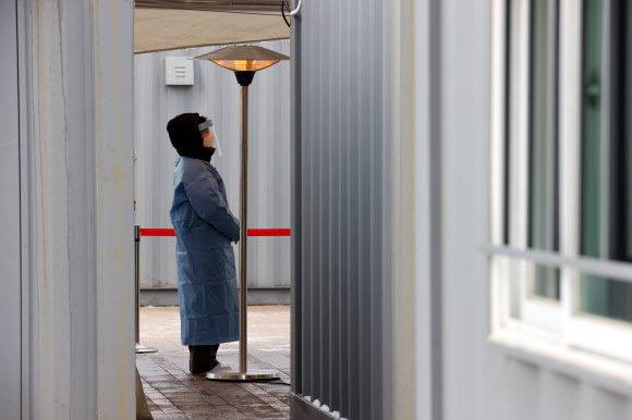 지난 13일 오전 서울시청 앞 마련된 임시선별진료소에서 의료진이 난로 아래 추위를 녹이며 검사자들을 기다리고 있다. 연합뉴스