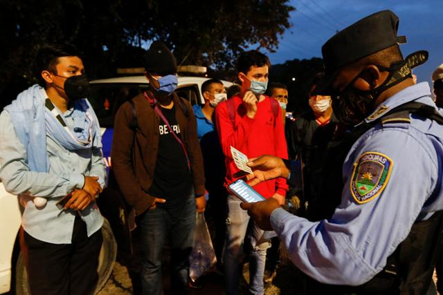 온두라스 산페드로술라에서 촐로마로 가는 고속도로에서 14일 도로를 봉쇄한 경찰들이 국경으로 이동하는 것을 허가하기 전 이민자들의 서류를 확인하고 있다. 산페드로술라=AP 연합뉴스
