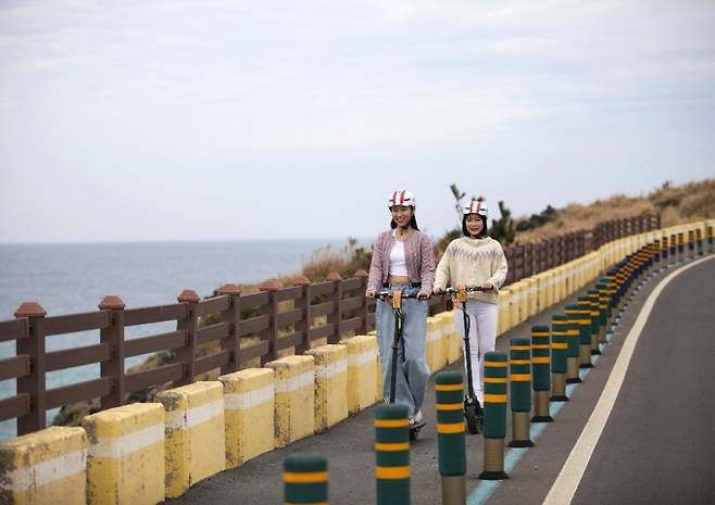 이브이패스에서 개발한 전원제어 스마트헬멧을 쓴 청년들이 이브이패스 공유전동킥보드를 타고 제주 해안로를 라이딩하고 있다.&nbsp;